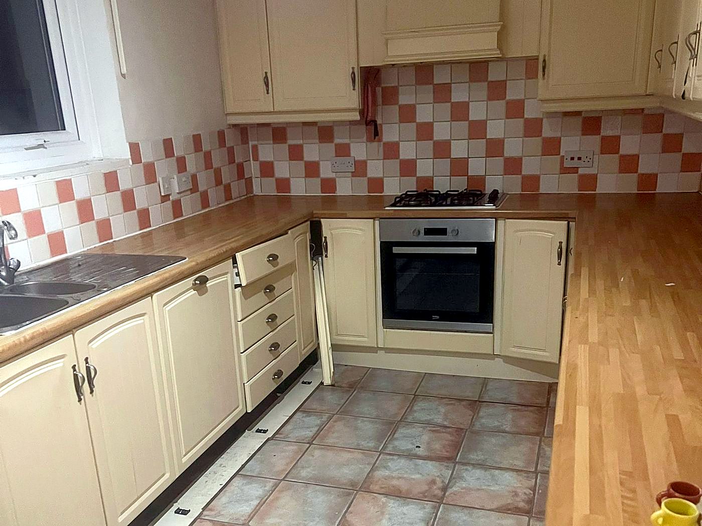 A kitchen before: cream units, orange and white tiles and a worn tiled floor
