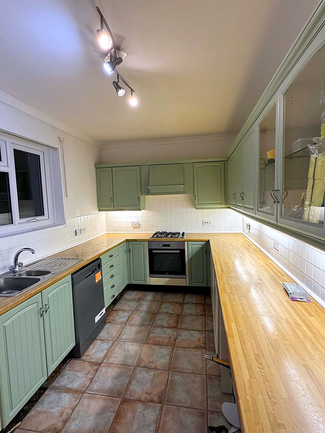 The same kitchen mid-works: units repainted sage green and tiles painted white